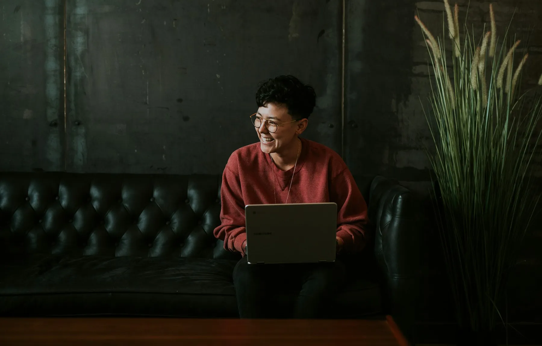 Mujer sonriendo mientras usa su laptop, con luz cálida sobre un sillón oscuro